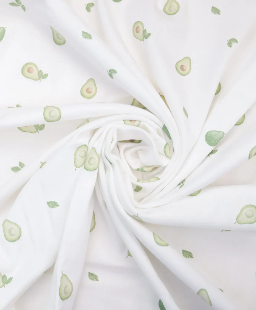 Organic cotton baby swaddle wrap with avocado print on white fabric, folded to display lightweight breathable material